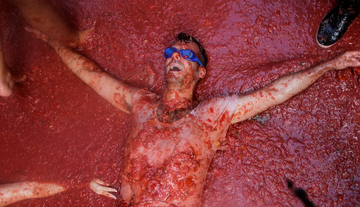 Seorang peserta Festival Tomatina tidur di jalan yang penuh dengan tomat di Bunol, Valencia, Spanyol, Rabu (31/8). Dalam festival tersebut warga lokal dan turis berbaur di jalanan dan saling melempar tomat. (REUTERS / Heino Kalis)