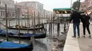 Orang-orang melihat gondola berlabuh di sepanjang kanal saat air surut di Venesia, Italia, 21 Februari 2023. Para ilmuwan dan kelompok lingkungan memperingatkan Pegunungan Alpen menerima kurang dari setengah dari hujan salju normalnya. (AP Photo/Luigi Costantini)