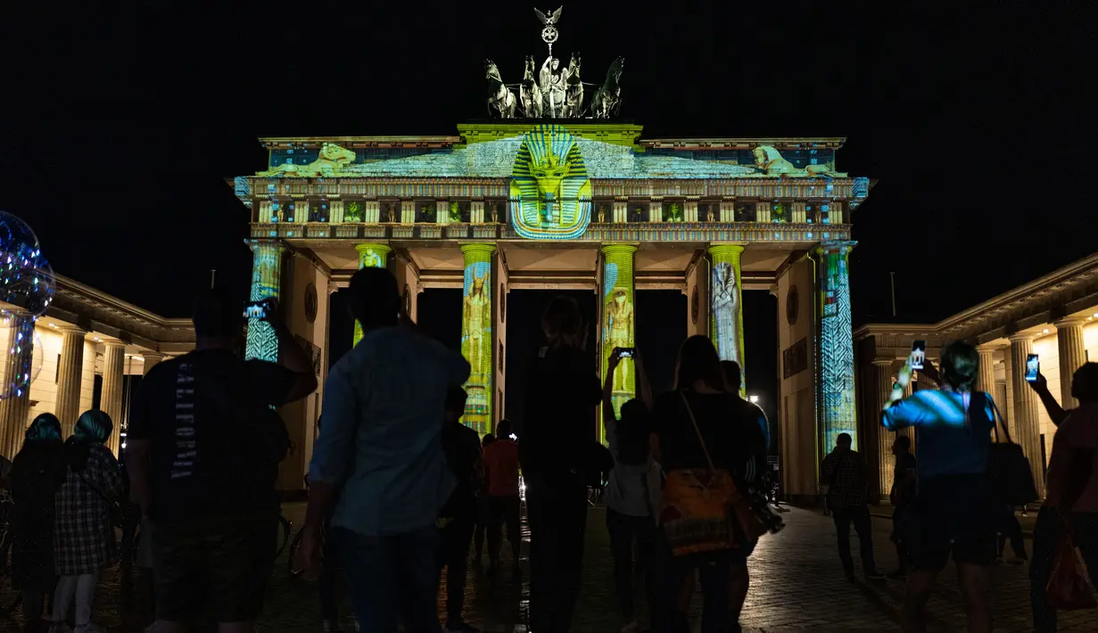 Orang-orang mengambil foto Gerbang Brandenburg yang diterangi cahaya dalam Festival of Lights di Berlin pada 14 September 2020. Kreasi cahaya lebih dari 90 karya seni tersebut ditampilkan di 86 lokasi yang berlangsung hingga 20 September mendatang. (John MACDOUGALL/AFP)