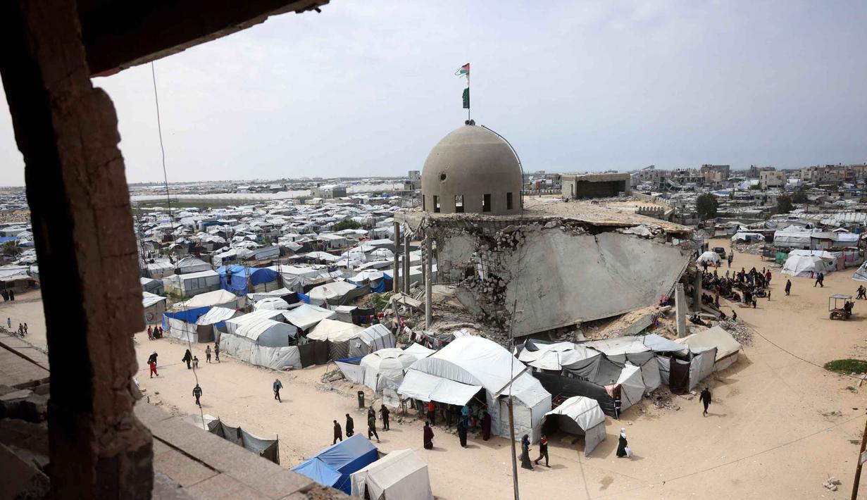 Kondisi bangunan yang nyaris rata dengan tanah dan miring, tidak menyurutkan niat mereka untuk tetap beribadah di lokasi tersebut. Tampak dalam foto, umat Muslim Palestina berdoa saat salat Jumat terakhir di bulan suci Ramadan 1447 Hijriah, di luar Masjid Al-Talbani, yang dihancurkan oleh militer Israel di Khan Yunis, Jalur Gaza selatan pada Jumat 13 Maret 2026. (Bashar Taleb/AFP)
