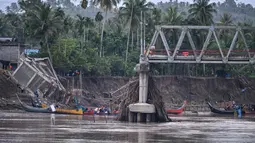 Sisa rangka jembatan terlihat menggantung di atas aliran sungai Peusangan yang masih deras. Tampak dalam foto, perahu-perahu yang digunakan untuk mengangkut penumpang menyeberangi Sungai Peusangan terlihat melewati jembatan yang runtuh di Kuta Blang, Kabupaten Bireuen, Provinsi Aceh, Selasa 9 Desember 2025. (CHAIDEER MAHYUDDIN/AFP)
