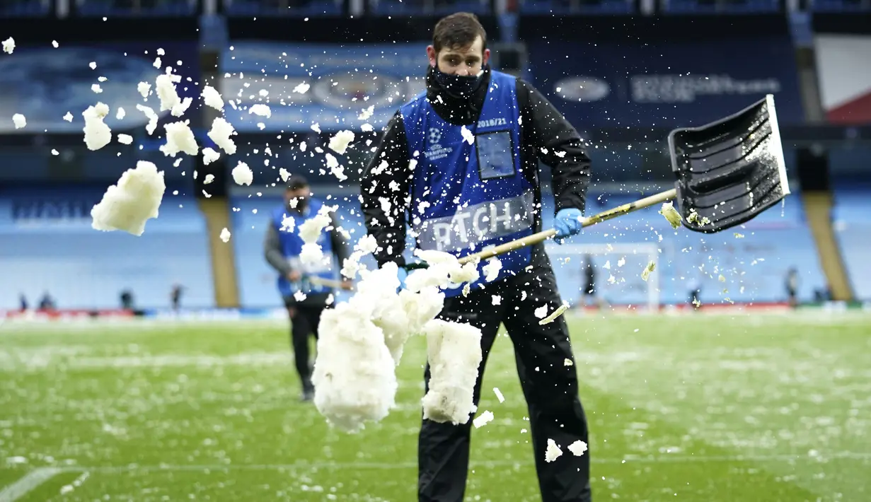 Petugas membuang salju yang menutupi rumput ke pinggir lapangan jelang laga Manchester City melawan PSG pada laga semifinal Liga Champions di Stadion Etihad, Rabu (5/5/2021). (AP/Dave Thompson)