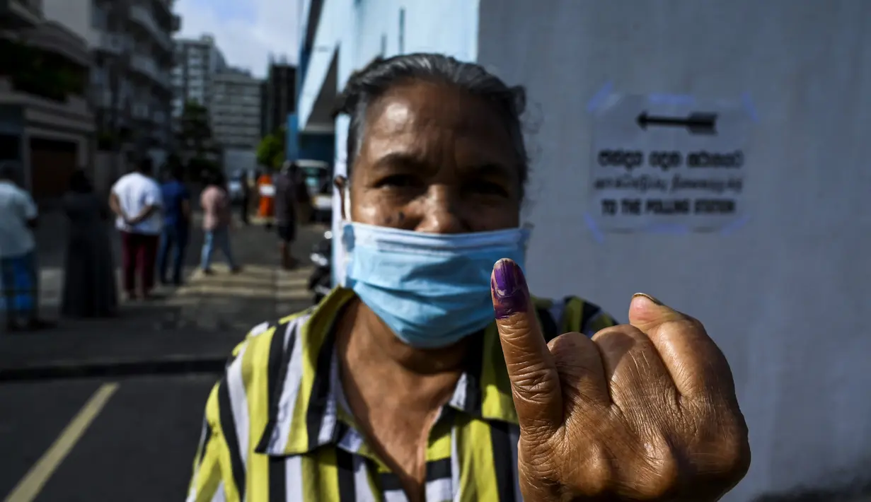 Seorang pemilih mengenakan masker menunjukkan jarinya yang bertinta usai melakukan pemungutan suara di Kolombo, Sri Lanka, Rabu (5/8/2020). Sri Lanka menggelar pemilihan parlemen di tengah pandemi COVID-19. (Ishara S. KODIKARA/AFP)