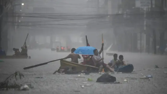 Tim penyelamat mendayung perahu mereka di sepanjang jalan yang banjir di ibu kota Filipina, Manila. [Ted Aljibe/AFP]
