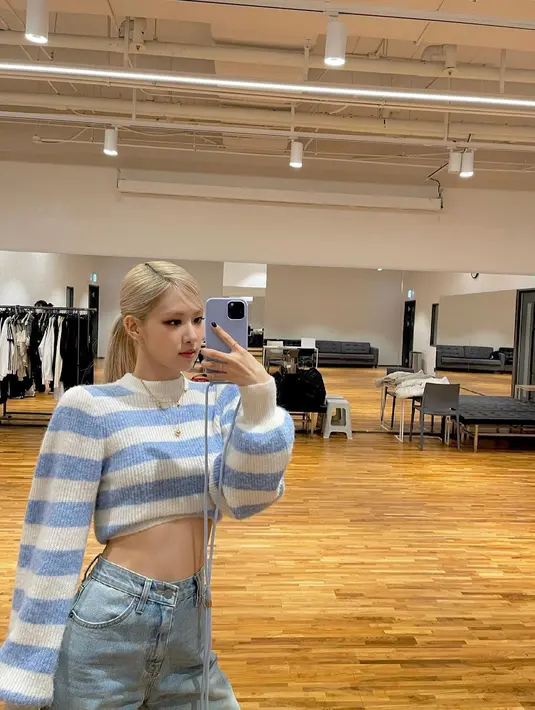 Saat mirror selfie, Rose BLACKPINK mengenakan sweater wol merino dan alpaka garis-garis warna biru pastel dengan aksen lengan balon seharga Rp4,2 juta. Sweater dari brand lokal Korea, Ganni ini di-styling gaya crop dan dipadukan dengan Jeans.