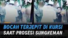 Seorang bocah laki-laki terjepit di kursi saat seorang perempuan dewasa tengah memeluk sang pengantin pria.