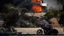 Seorang pria mengendarai motor melewati sebuah rumah yang terkena dampak kebakaran di Ventura, California, AS (5/12). Dipicu oleh angin kencang Santa Ana, api merambat dengan cepat dan merusak sekitar 26.000 hektare. (AP Photo / Noah Berger)