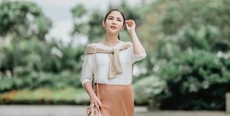 Tampilan feminin yang stylish, padukan long sleeve dengan satin flare skirt warna peach. Makin stylish dengan cardigan yang diikat di pundak. (Instagram/jscmila).