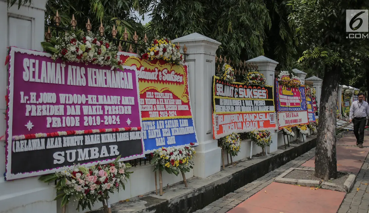 Pejalan kaki melintasi karangan bunga bertuliskan ucapan selamat untuk Joko Widodo (Jokowi) dan Ma'ruf Amin di gedung Sekretariat Negara, Jakarta, Senin (22/4). Karangan bunga dari pendukung Jokowi-Ma'ruf tersebut ditujukan atas kemenangan pasangan itu pada Pilpres 2019. (Liputan6.com/Faizal Fanani)