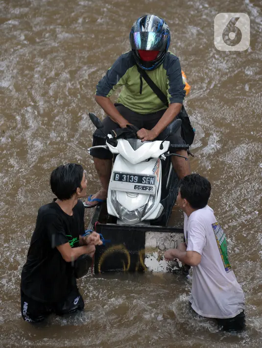 Pengendara sepeda motor menaiki gerobak saat melintasi banjir yang merendam Jalan Kapten Tendean, Jakarta, Sabtu (20/2/2021). Banjir yang disebabkan curah hujan tinggi memutus akses lalu lintas di Jalan Kapten Tendean. (merdeka.com/Imam Buhori)