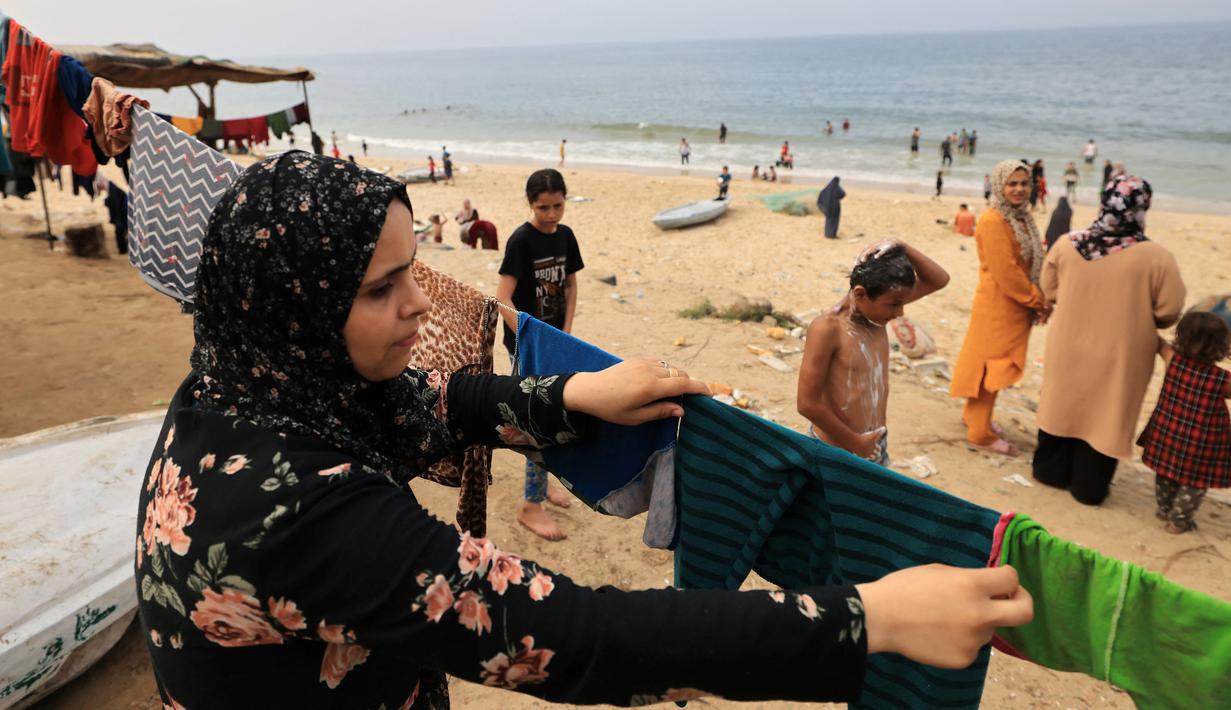 Seorang perempuan Palestina menggantung cucian yang dicuci menggunakan air laut karena kurangnya air bersih dan listrik di sepanjang pantai di Deir el-Balah di selatan Jalur Gaza, di tengah pertempuran yang sedang berlangsung antara Israel dan kelompok Palestina Hamas. pada 29 Oktober 2023. (MAHMUD HAMS / AFP)