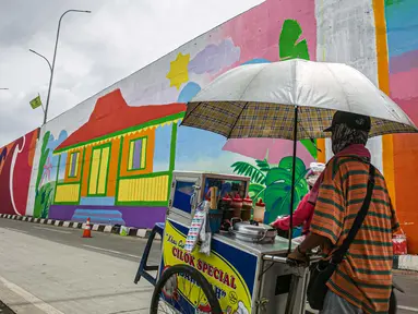 Seorang pedagang melintasi mural yang dibuat di Flyover Gaplek, Tangerang Selatan, Rabu (10/3/2021). Konsep muralnya adalah "Tangsel Membangun". (Liputan6.com/Faizal Fanani)