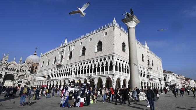 Wisatawan berjalan melintasi Lapangan Santo Markus dengan latar Basilika Santo dan Istana Doge di Venesia, Italia (4/11/2019). (AFP Photo/Miguel Medina)