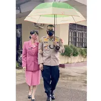 Di bawah payung, Uut tampil anggun mengenakan pakaian Bhayangkari dengan ciri khas pinknya. Mulai dari kemeja, blazer, hingga skirtnya. Ia memadukannya dengan flat shoes hitam. (@uutpermatasari)
