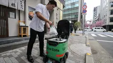 Seorang karyawan restoran menempatkan pesanan makanan di dalam robot tanpa awak selama uji coba layanan pengiriman robot oleh Uber Eats Japan, Mitsubishi Electric dan pengembang robot Cartken di pusat kota Tokyo pada tanggal 5 Maret 2024. (Richard A. Brooks/AFP)