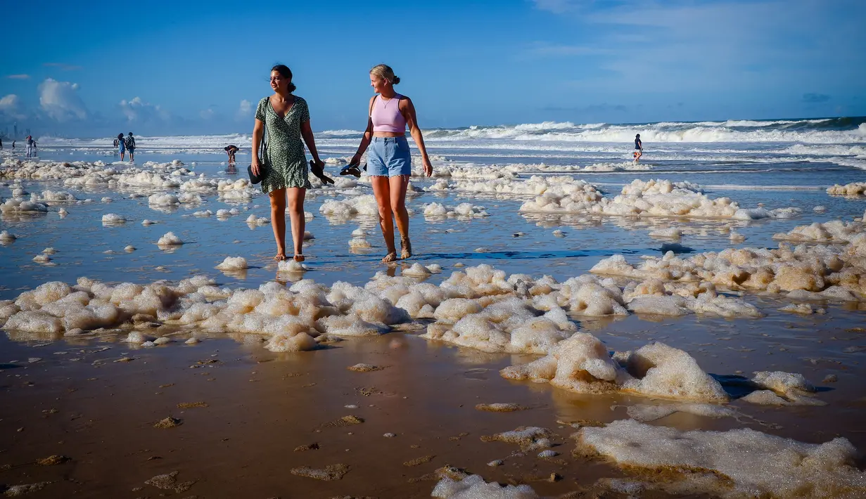 Wisatawan berjalan di antara busa pantai setelah siklon tropis di Currumbin Beach, Gold Coast, Australia pada 15 Desember 2020. Hujan lebat dan angin kencang telah melanda kawasan perbatasan padat penduduk antara New South Wales dan Queensland selama tiga hari. (Photo by Patrick HAMILTON / AFP)
