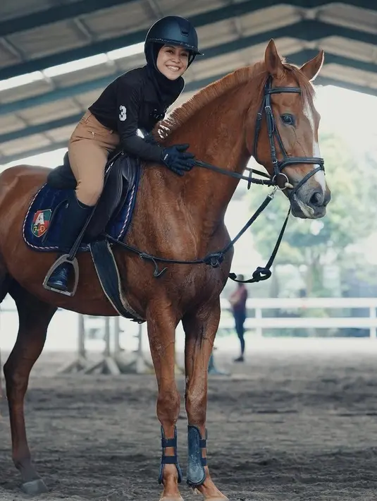 Saat berkuda, ia nampak mengenakan atasan hitam lengan panjang dan celana coklatnya, lengkap mengenakan sepatu boots dan helmnya. (@lestykejora)