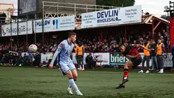 Pemain Tamworth, Kai Williams (kanan) melakukan umpan silang dibayangi pemain Tottenham Hotspur pada laga Piala FA 2024/2025 di The Lamb Ground, Tamworth, Inggris, Minggu (12/01/2025) waktu setempat. (AFP/Henry Nicholls)