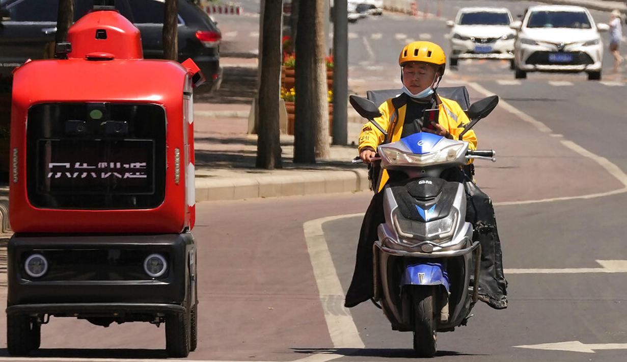 Seorang petugas pengiriman melewati kendaraan pengiriman otonom dari JD.com di jalanan Beijing, China, Jumat (28/5/2021). Raksasa e-commerce China JD.com meningkatkan operasi kendaraan pengiriman tak berawak. (AP Photo/Ng Han Guan)