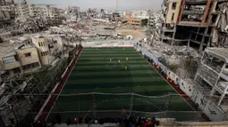 Sebuah pertandingan sepak bola lima lawan lima menarik perhatian warga Palestina di tengah kekerasan yang terus berlanjut di wilayah Gaza. Tampak dalam foto, warga Palestina menyaksikan pertandingan sepak bola lima lawan lima di tengah reruntuhan bangunan yang hancur di Kota Gaza pada Senin 9 Februari 2026. (Omar AL-QATTAA/AFP)