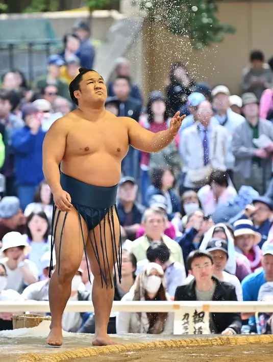 Seorang pegulat sumo melemparkan tanah ke udara sebelum bertanding dalam turnamen Honozumo di Kuil Yasukuni, Tokyo, Jepang, 15 April 2019. Ribuan penonton dari dalam dan luar negeri menikmati pertandingan dalam turnamen tersebut. (TRIBALLEAU CHARLY/AFP)