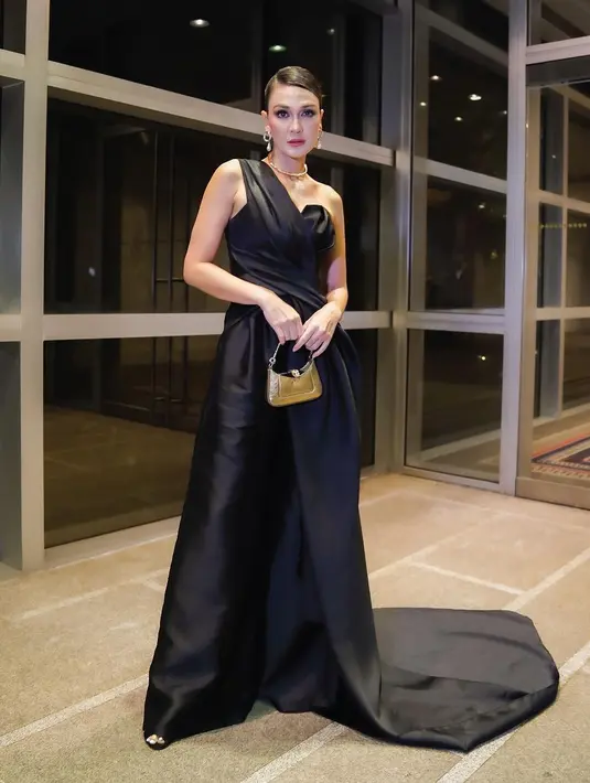 Penampilan Luna Maya dengan sebuah jumpsuit dress hitam yang glamor. Jumpsuit ini memiliki bagian top yang asimetris dan bagian roknya menjuntai hingga ke lantai. Penampilannya dipermanis dengan mini bag bernuansa emas yang ditentengnya. [Foto: Instagram/lunamaya]