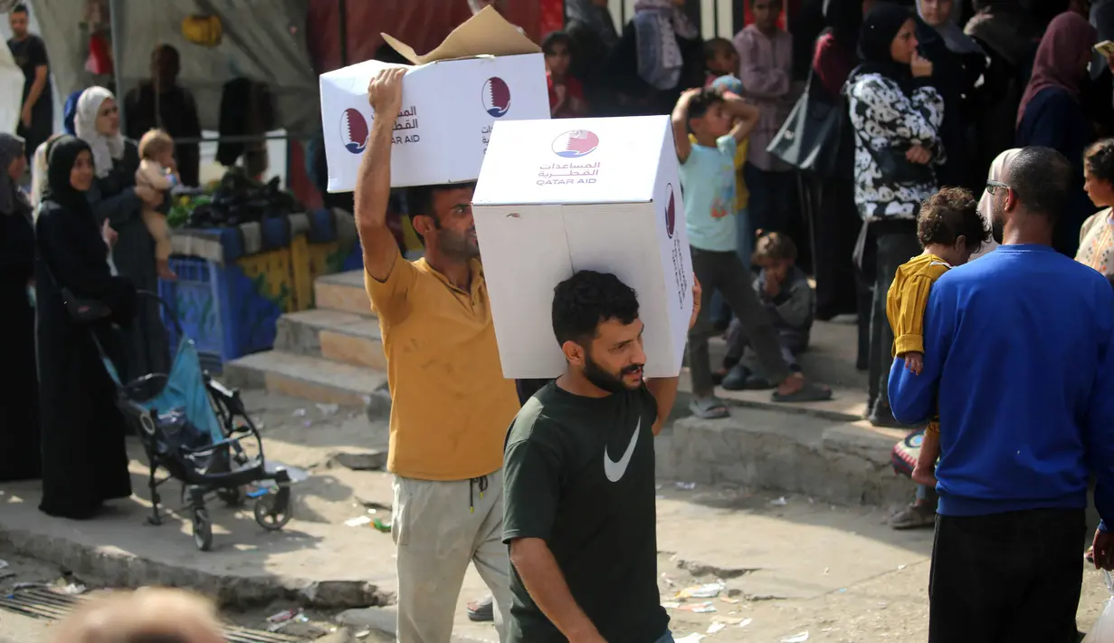 Pria-pria Palestina masing-masing membawa satu kotak makanan, yang dikumpulkan di pusat distribusi di kamp pengungsi Nuseirat, di pusat Jalur Gaza pada 2 November 2025. PBB menegaskan bahwa semua pihak harus menahan diri dari tindakan yang dapat membahayakan warga sipil dan pekerja kemanusiaan. (EYAD BABA/AFP)