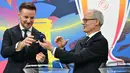 Melalui pengundian ini, setiap tim akan mengetahui potensi lawan mereka selanjutnya. Tampak dalam foto, Wakil Sekretaris Jenderal UEFA Giorgio Marchetti (kanan) menyerahkan bola undian kepada duta Yayasan UEFA untuk Anak-Anak yang juga mantan gelandang Sevilla, Ivan Rakitic, selama pengundian babak 16 besar, perempat final, dan semifinal Liga Champions 2025/2026 di House of European Football di Nyon, Swiss, Jumat (27/2/2026). (Harold CUNNINGHAM/AFP)