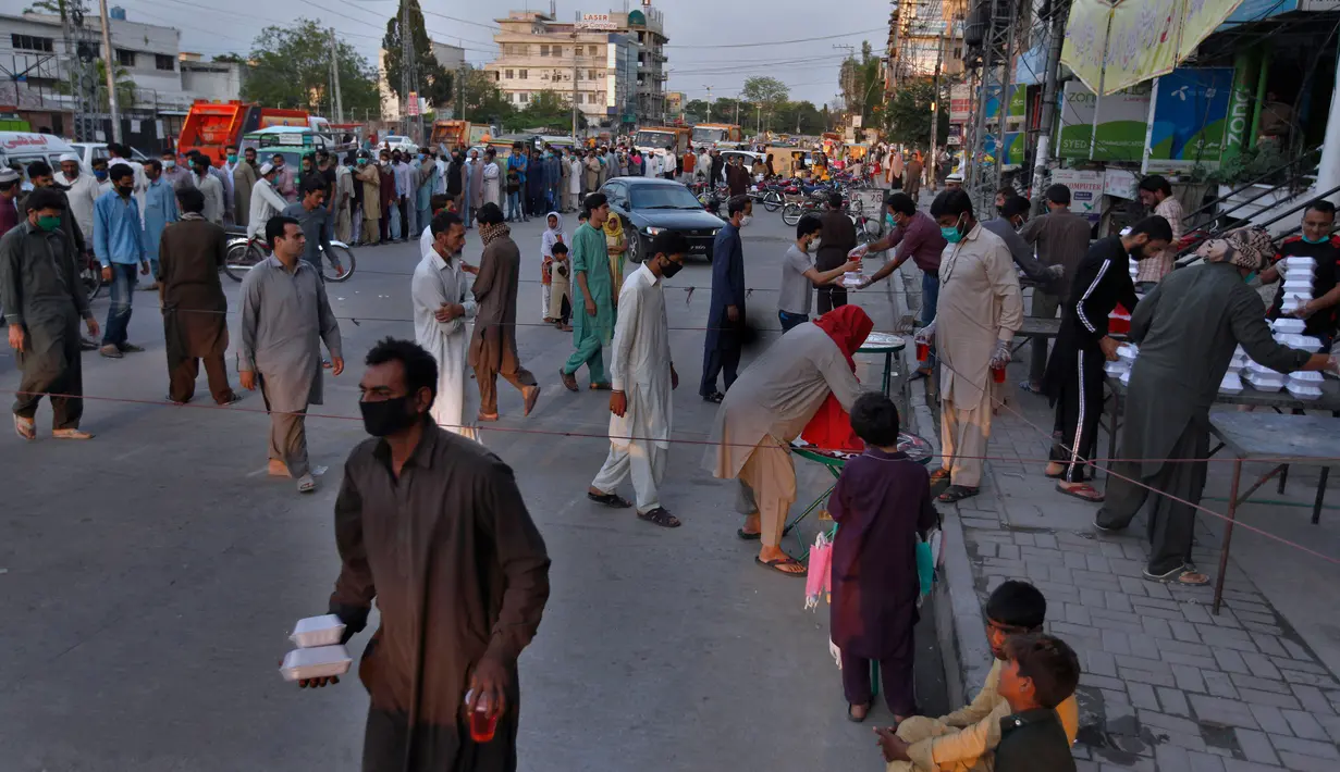 Orang-orang menerima kotak makanan dan minuman manis tradisional untuk berbuka puasa di Rawalpindi, Pakistan, Minggu, (3/5/2020). Umat Muslim di seluruh dunia sedang melaksanakan Ramadan untuk menahan diri dari makan, minum sejak subuh sampai senja. (AP/Anjum Naveed)