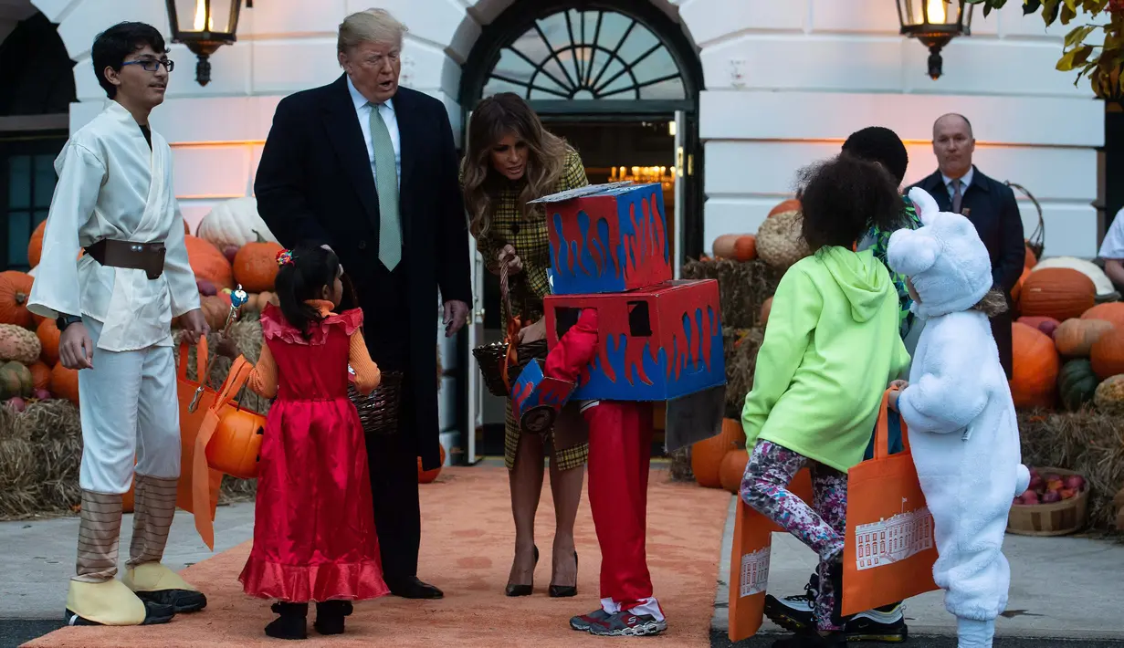Presiden Amerika Serikat (AS) Donald Trump dan Ibu Negara Melania Trump membagikan permen kepada anak-anak selama yang hadir acara trick-or-treat pada perayaan Halloween di Gedung Putih, Washington, Minggu (28/10). (NICHOLAS KAMM / AFP)