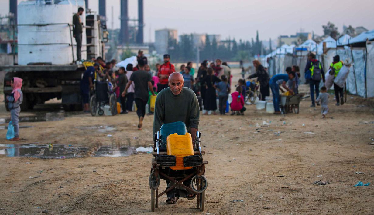 Laporan Perserikatan Bangsa Bangsa (PBB) per Oktober 2025 menyebutkan bahwa sekitar 84% infrastruktur di Gaza, termasuk jaringan air bersih, telah hancur. Pipa-pipa utama rusak parah, menyebabkan jaringan distribusi air lumpuh. Tampak dalam foto, orang-orang mengisi wadah air mereka di kamp Nuseirat untuk pengungsi Palestina di Jalur Gaza tengah pada Kamis 4 Desember 2025. (Eyad Baba/AFP)