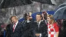 Presiden Rusia Vladimir Putin (kiri) bersama Presiden Prancis Emmanuel Macron (tengah) dan Presiden Kroasia Kolinda Grabar-Kitarovic berjalan dalam hujan usai laga final Piala Dunia 2018 di Stadion Luzhnik, Moskow, Rusia, Minggu (15/7). (Franck Fife/AFP)