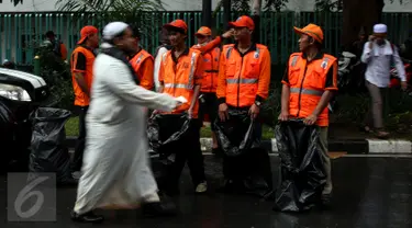 Seorang pejalan kaki melewati sejumlah pasukan oranye (petugas kebersihan) yang disiagakan di kawasan Monas, Jakarta, Jumat (2/12). Pasukan oranye disiagakan untuk menjaga kebersihan lingkungan saat aksi damai 2 Desember. (Liputan6.com/Johan Tallo)