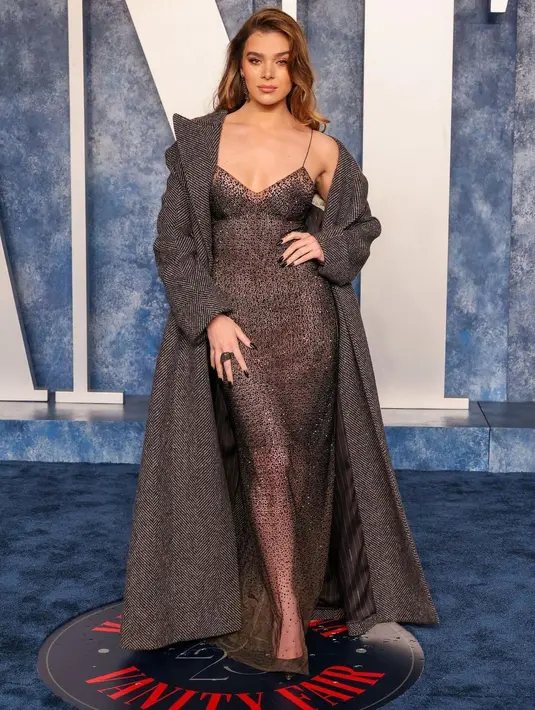 Hailee Steinfeld tampil mewah dalam balutan gaun strap spaghetti tembus pandang yang dipadukan dengan maxi coat. [Foto: IG/haileesteinfeld].