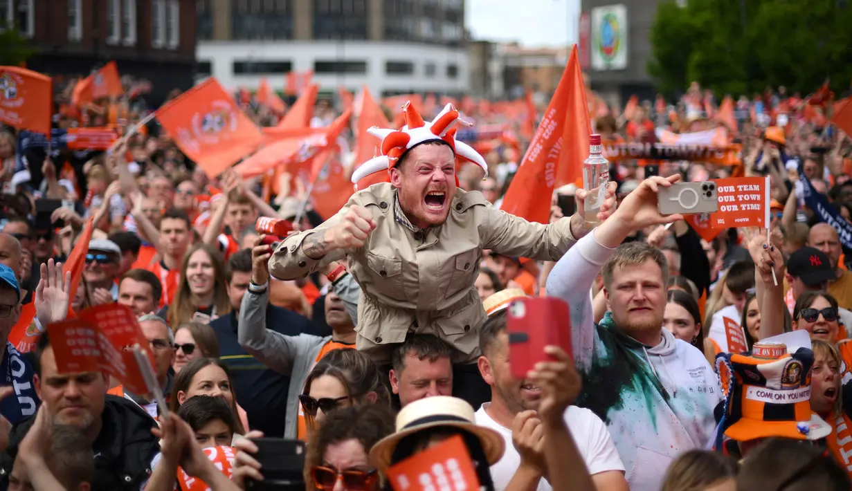 Pendukung Luton Town menyambut kedatangan parade bus timnya melewati jalanan di Luton, Inggris setelah berhasil promosi ke Liga Inggris musim 2023/2024 pada Senin (29/05/2023) waktu setempat. The Hatters sukses menyegel tiket promosi setelah memenangkan laga play-off divisi Championship melawan Covetry City 6-5 melalui adu penalti di Wembley, Sabtu (27/5/2023). (AFP/Daniel Leal)