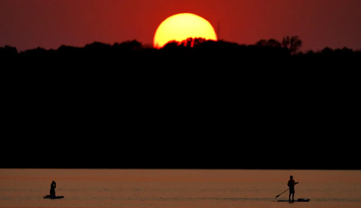 Orang-orang menyaksikan matahari terbenam sambil berperahu di Shawnee Mission Lake, Shawnee, Kansas, Amerika Serikat, Jumat (9/10/2020). Matahari terbenam terus lebih cerah dari biasanya karena asap dari kebakaran hutan barat terus melayang di seluruh negeri. (AP Photo/Charlie Riedel)