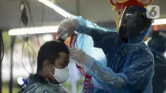 Tukang cukur mengenakan alat pelindung diri (APD) dari plastik saat mencukur rambut pelanggan di Pondok Kelapa, Jakarta, Selasa (5/5/2020). Tukang cukur mengenakan APD untuk mengurangi risiko penularan virus corona COVID-19. (merdeka.com/Imam Buhori)