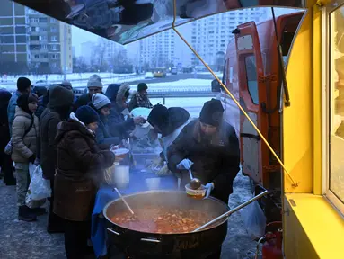 Para sukarelawan dari organisasi amal makanan yang berbasis di Amerika Serikat (AS), World Central Kitchen, membagikan makanan hangat kepada warga setempat di sebuah kawasan perumahan di Kyiv yang mengalami pemadaman listrik dan air akibat serangan Rusia yang menghantam sektor energi, Kamis 22 Januari 2026. Serangan Rusia yang menghantam sektor energi melumpuhkan pasokan pemanas, listrik, dan air di ribuan bangunan permukiman di ibu kota Ukraina, Kyiv, ketika suhu udara turun hingga minus 14 derajat Celsius. (Sergei GAPON/AFP)
