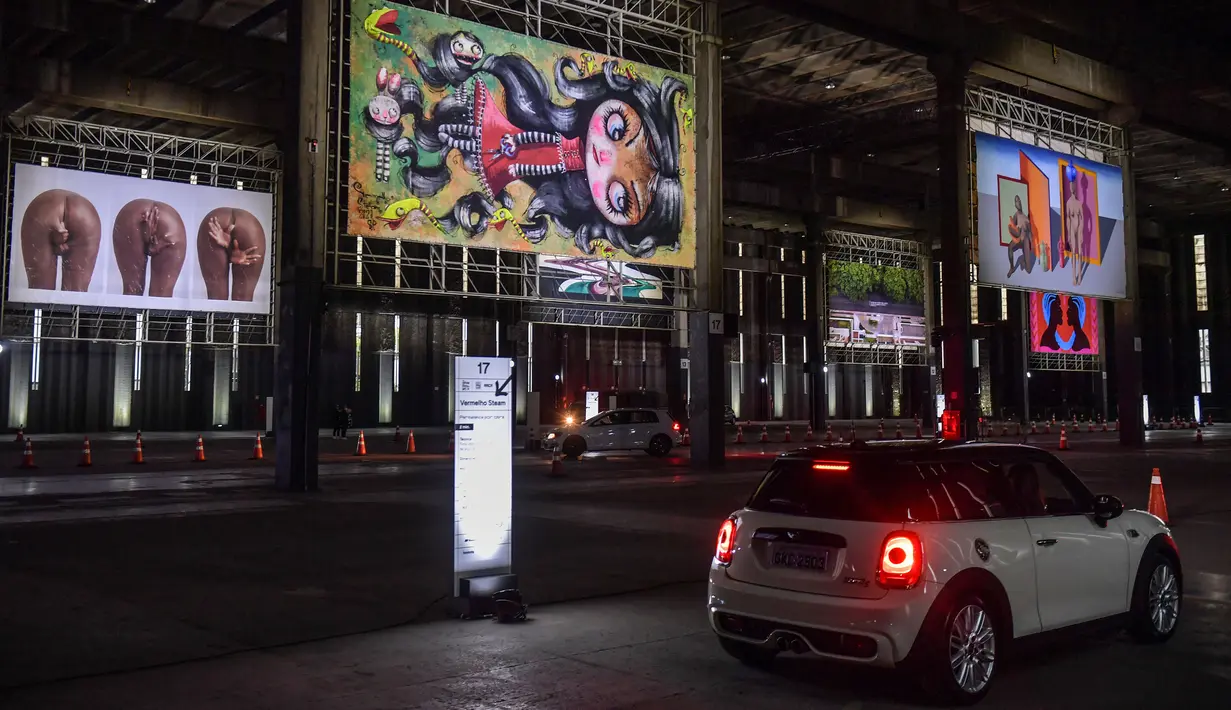 Orang-orang mengunjungi pameran seni dengan mengendarai mobil mereka melintasi gudang yang memajang lukisan dan foto di Sao Paulo pada 30 Juli 2020. Dengan galeri-galeri dan museum ditutup akibat pandemi virus corona, pemilik galeri seni Brasil meresmikan pameran drive-thru. (NELSON ALMEIDA/AFP)