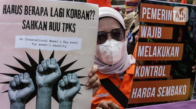 Buruh perempuan memegang poster saat menggelar aksi di depan gedung DPR RI, Jakarta, Selasa (8/3/2022). Mereka menuntut dibatalkannya Omnibus Law UU Cipta Kerja dan mendesak agar RUU Tindak Pidana Kekerasan Seksual (TPKS) segera disahkan oleh DPR RI. (Liputan6.com/Johan Tallo)