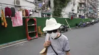 Seorang warga yang mengenakan masker berjalan melewati penghalang di sekitar komunitas di Shanghai (2/6/2022). Lalu lintas, pejalan kaki dan pelari muncul kembali di jalan-jalan Shanghai ketika kota terbesar di China mulai kembali normal di tengah pelonggaran penguncian COVID-19 dua bulan yang ketat atas penerapannya. (AP Photo/Ng Han Guan)