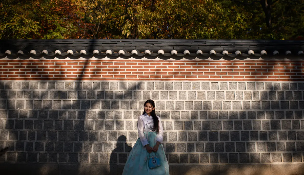 Seorang wanita mengenakan pakaian tradisional hanbok berpose saat difoto di bawah pohon ginkgo di istana Gyeongbokgung di Seoul (31/10). Pohon ini dikenali mirip dengan fosil 270 juta tahun lalu. (AFP Photo/Ed Jones)