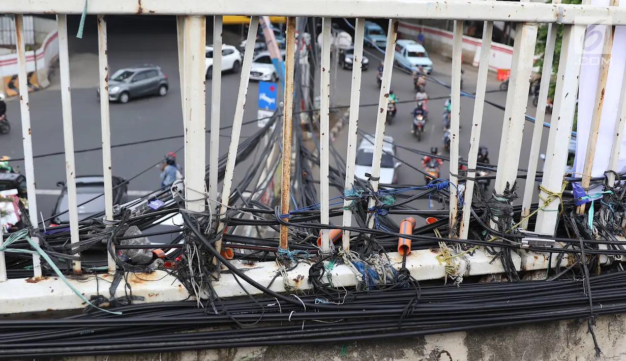 Instalasi kabel semrawut menjuntai di Jalan Dewi Sartika, Jakarta Timur, Sabtu (19/1). Selain mengganggu keindahan kota, kondisi tersebut juga berbahaya karena dapat memicu hubungan pendek arus listrik. (Liputan6.com/Immanuel Antonius)
