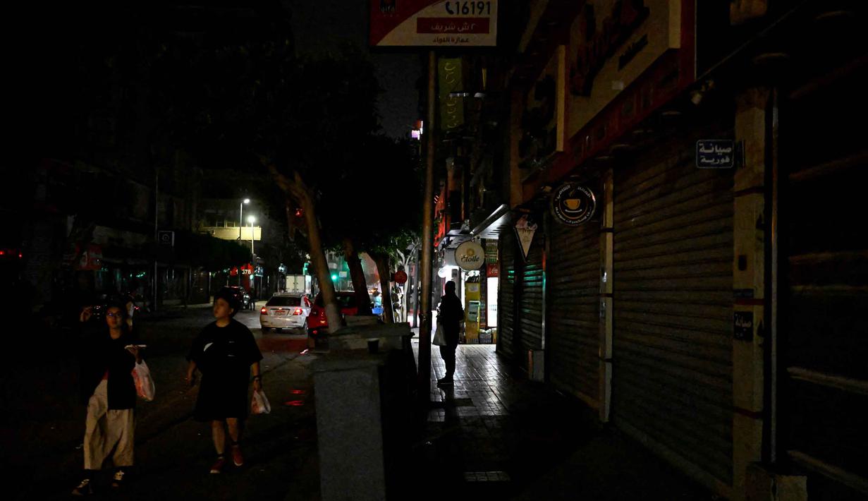 Saat ini, warga Kairo, Mesir, dipaksa untuk menyesuaikan diri dengan kota yang lebih gelap dan sepi demi menjaga ketahanan energi nasional. Tampak dalam foto, orang-orang berjalan melewati toko-toko yang tutup lebih awal karena jam malam yang diberlakukan pemerintah untuk mengurangi biaya energi di pusat kota Kairo, Mesir, pada Kamis 2 April 2026. (Khaled DESOUKI/AFP)
