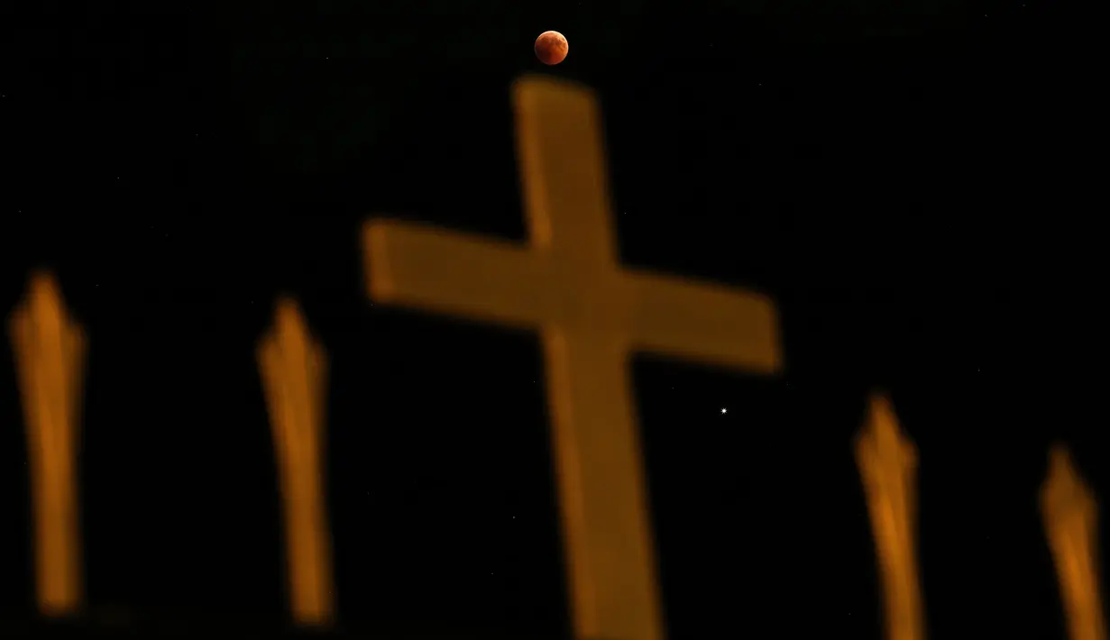 Fenomena gerhana bulan total "Micro Blood Moon" terlihat di atas salib gereja Ortodoks Kristen di Nicosia, Siprus, Jumat (27/7). Gerhana bulan yang terlama pada abad ini dapat disaksikan di seluruh dunia dengan mata telanjang. (AP/Petros Karadjias)