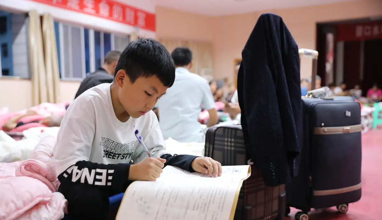 Seorang anak laki-laki mengerjakan tugas sekolahnya di tempat penampungan sementara di Bikou di Wilayah Wenxian, yang terletak di Kota Longnan, Provinsi Gansu, China barat laut (18/8/2020). (Xinhua/Chen Bin)