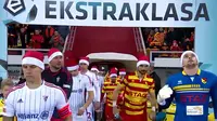 Para pemain kedua klub di Liga Polandia menggunakan topi natal dan mendapatkan kejutan dengan hadirnya sinterklas di tengah lapangan.