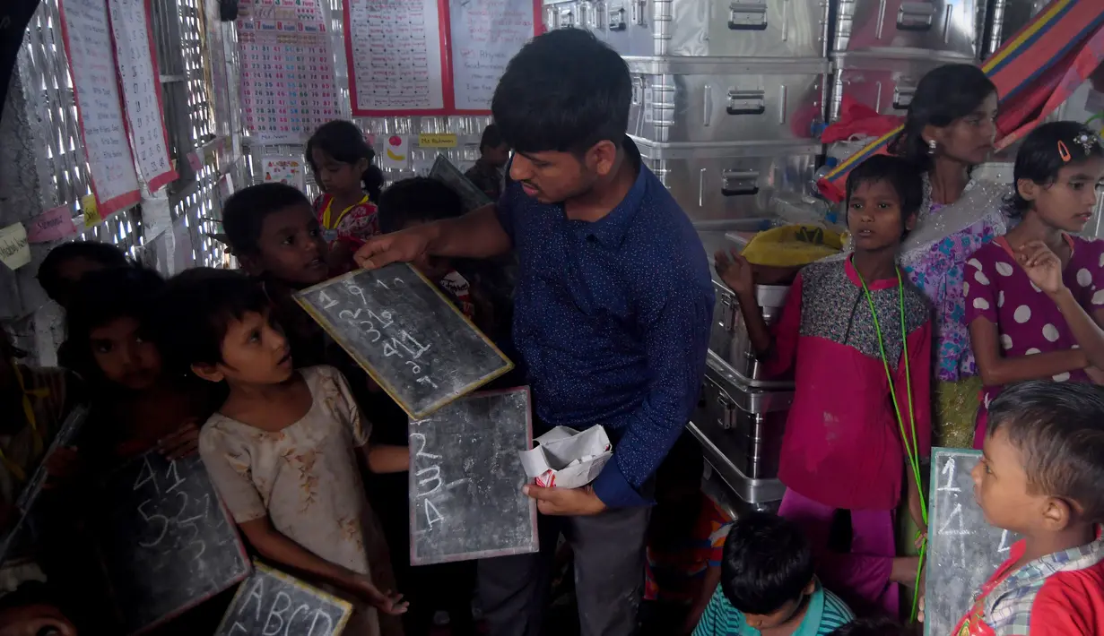 Seorang pengajar memeriksa tugas anak-anak Rohingya di sebuah sekolah darurat di kamp pengungsian di Teknaf, Bangladesh, 8 Oktober 2017. Sekelompok relawan mendirikan sekolah dan zona khusus untuk membantu bocah-bocah tersebut. (MUNIR UZ ZAMAN / AFP)