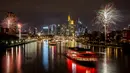 Kapal pesta berlayar mengarungi Sungai Main saat beberapa kembang api meledak dekat gedung-gedung di Frankfurt, Jerman, Sabtu (1/1/2022). Karena pandemi COVID-19, pesta kembang api tidak diperbolehkan. (Photo/Michael Probst)