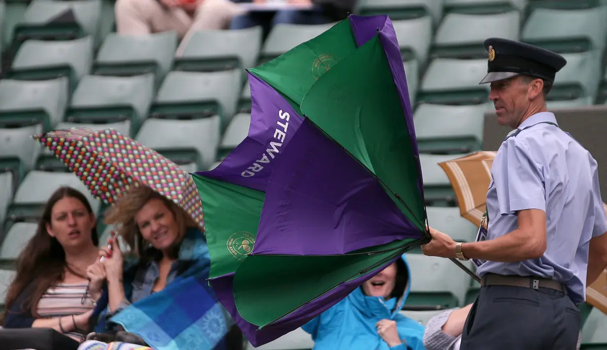Petugas berusaha membetulkan payung saat hujan turun dalam pertandingan perempat final wanita antara petenis Slovakia Magdalena Rybarikova dan pemain AS Coco Vandeweghe di kejuaraan Wimbledon 2017 di London (11/7). (AFP Photo/Daniel Leal Olivas)